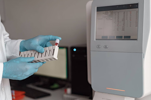A lab worker is inserting a tube of bloodwork into a machine.