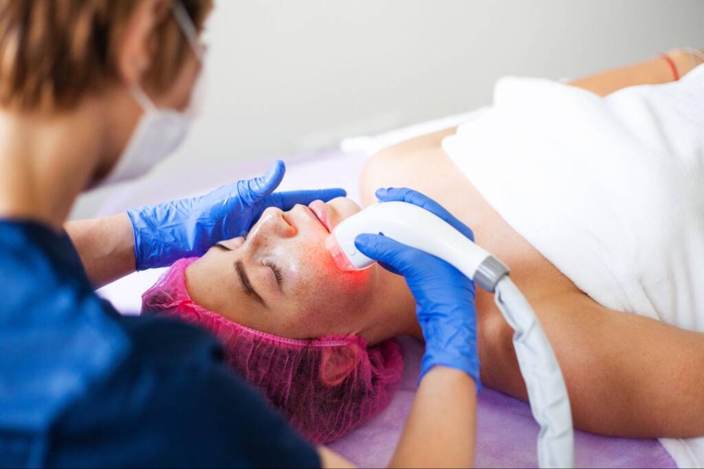 A woman is lying down and receiving laser treatments.