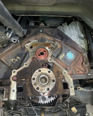 Close-up of a disassembled engine block showing the timing cover, gears, and oil residue, with various components and wires in the background.
