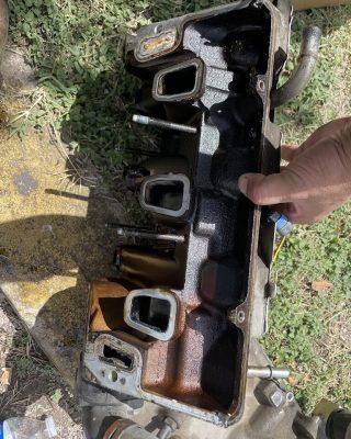 A person holds a valve cover while working on a car engine, focusing on maintenance or repair tasks.