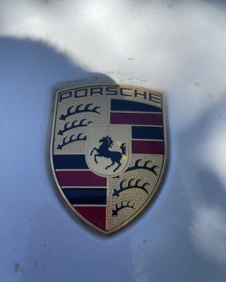Porsche emblem displayed on the hood of a sleek white car, showcasing luxury and performance.
