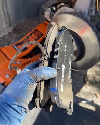 A person holds a brake pad while inspecting a car's braking system.
