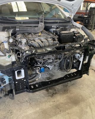 A car in a garage with its engine removed, revealing the empty engine bay and surrounding tools.