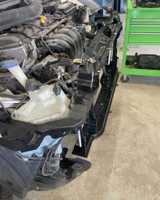 A car with its engine removed is resting on the ground inside a garage. Tools and parts are scattered around.