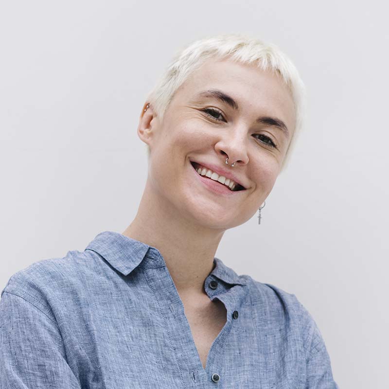 Woman looking at the camera with a nose ring, short blonde hair and wearing a blue shirt