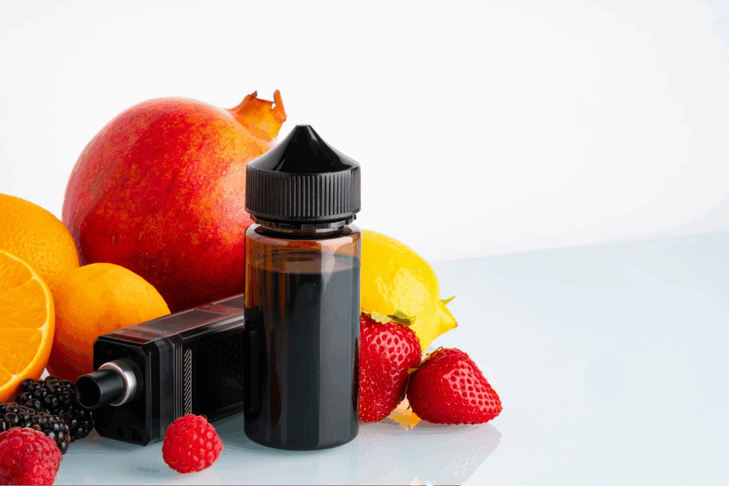 A bottle of vape juice and a vaping device surrounded by fruit against a white background.