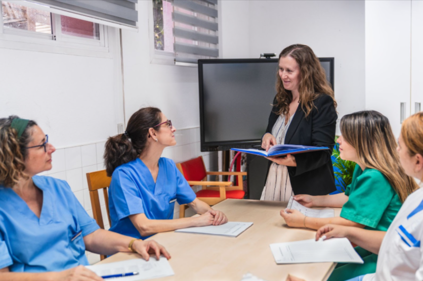 Staff nurses listen attentively as a nurse consultant facilitates a team discussion.