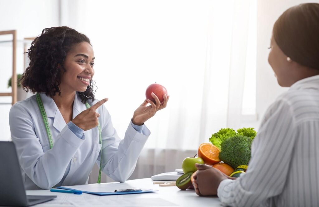 Female doctor holding an apple and speaking to a woman.