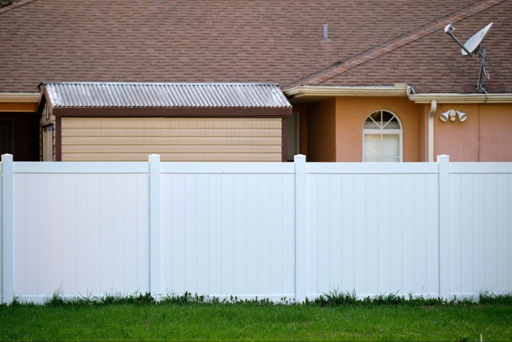 Vinyl fence next to grass, a shed, and a home.