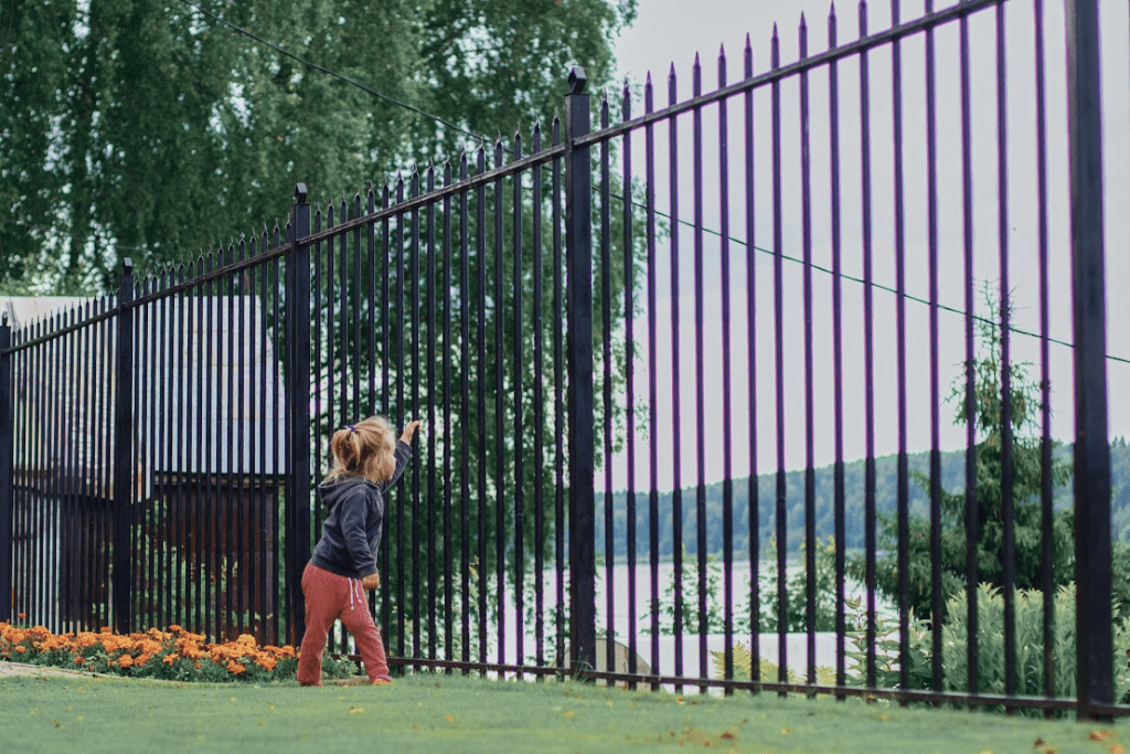 A child is leaning against an aluminum fence.