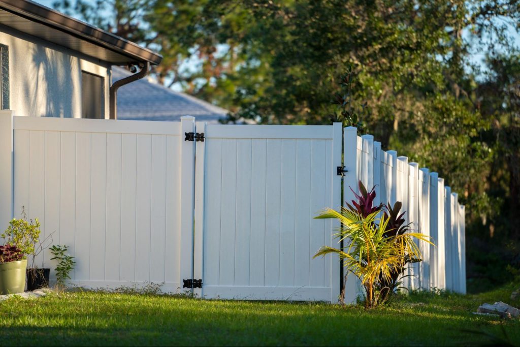 Vinyl fence with a gate next to a home and grass.