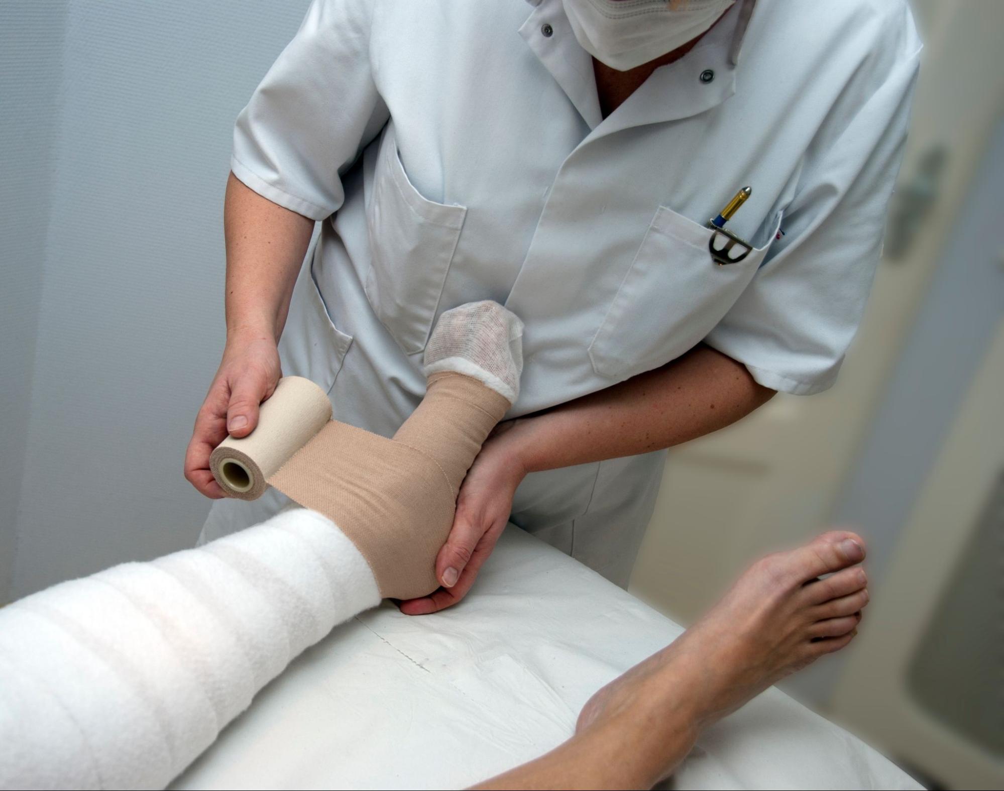 A nurse dressing a woman’s leg and foot in a hospital.