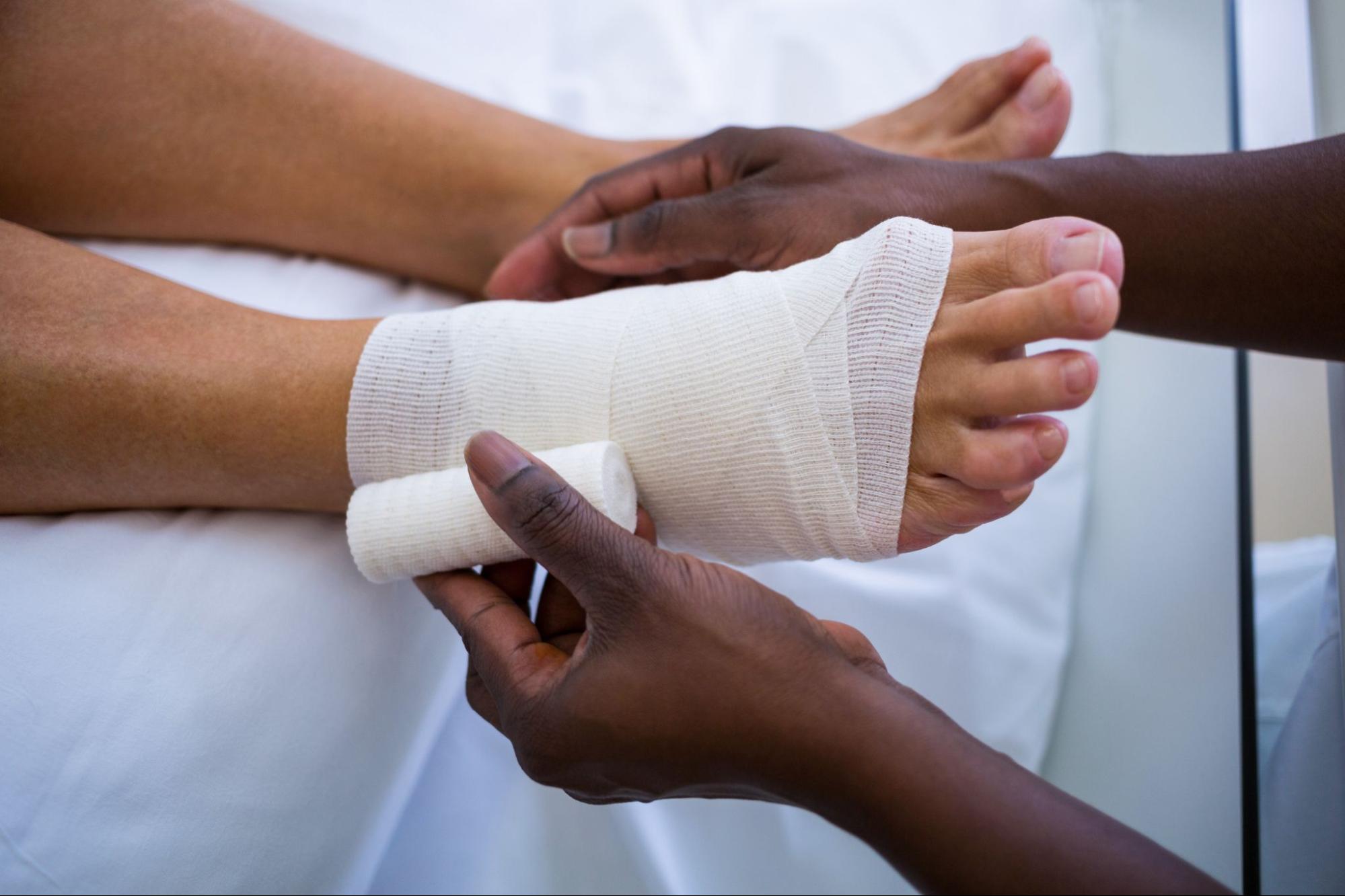 A nurse with medical gloves on dressing a wound on a man's foot. 