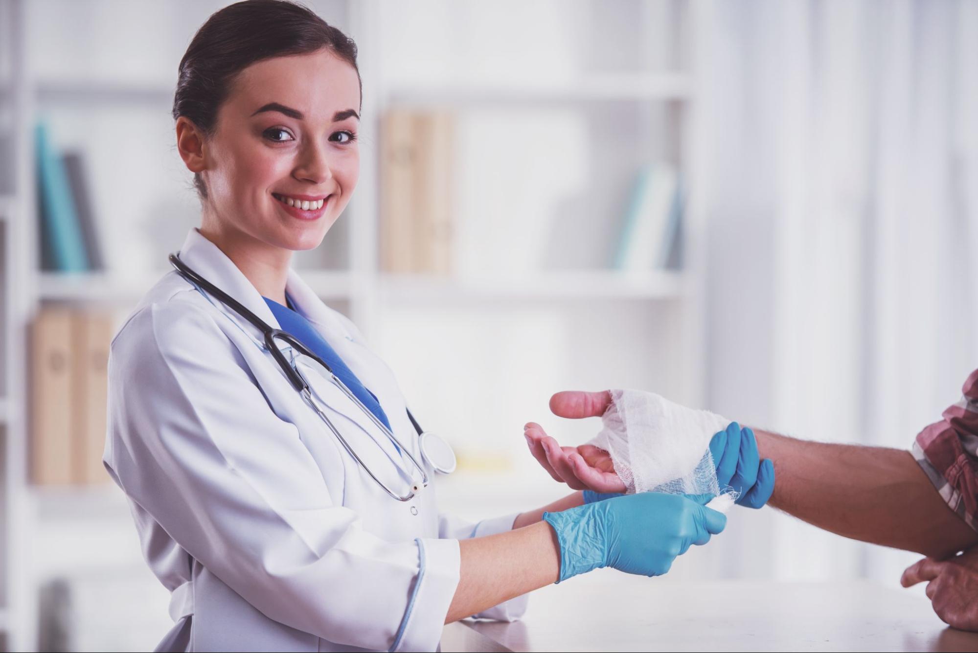 A female doctor bandaging the hand of a person.