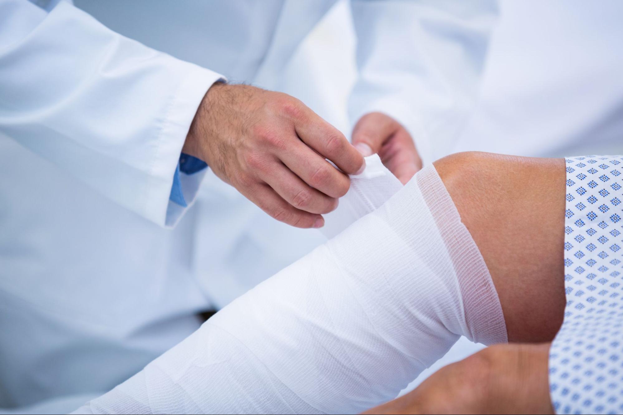 A doctor wrapping a patient’s leg with a white bandage.
