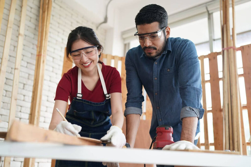 A couple works together in a wood workshop, building storage for their home improvement project.
