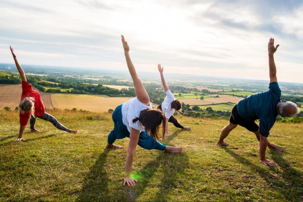 A group of people taking part in a spiritual practice outside on a grassy hill.