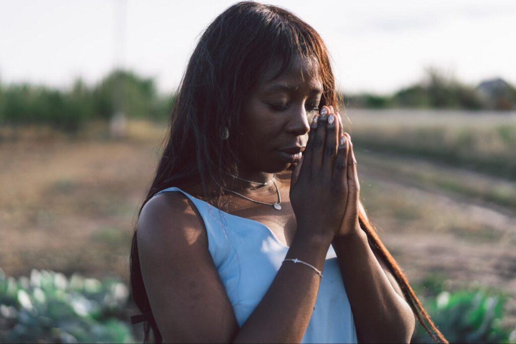 Peaceful moment of an Afro girl in prayer under the open sky.